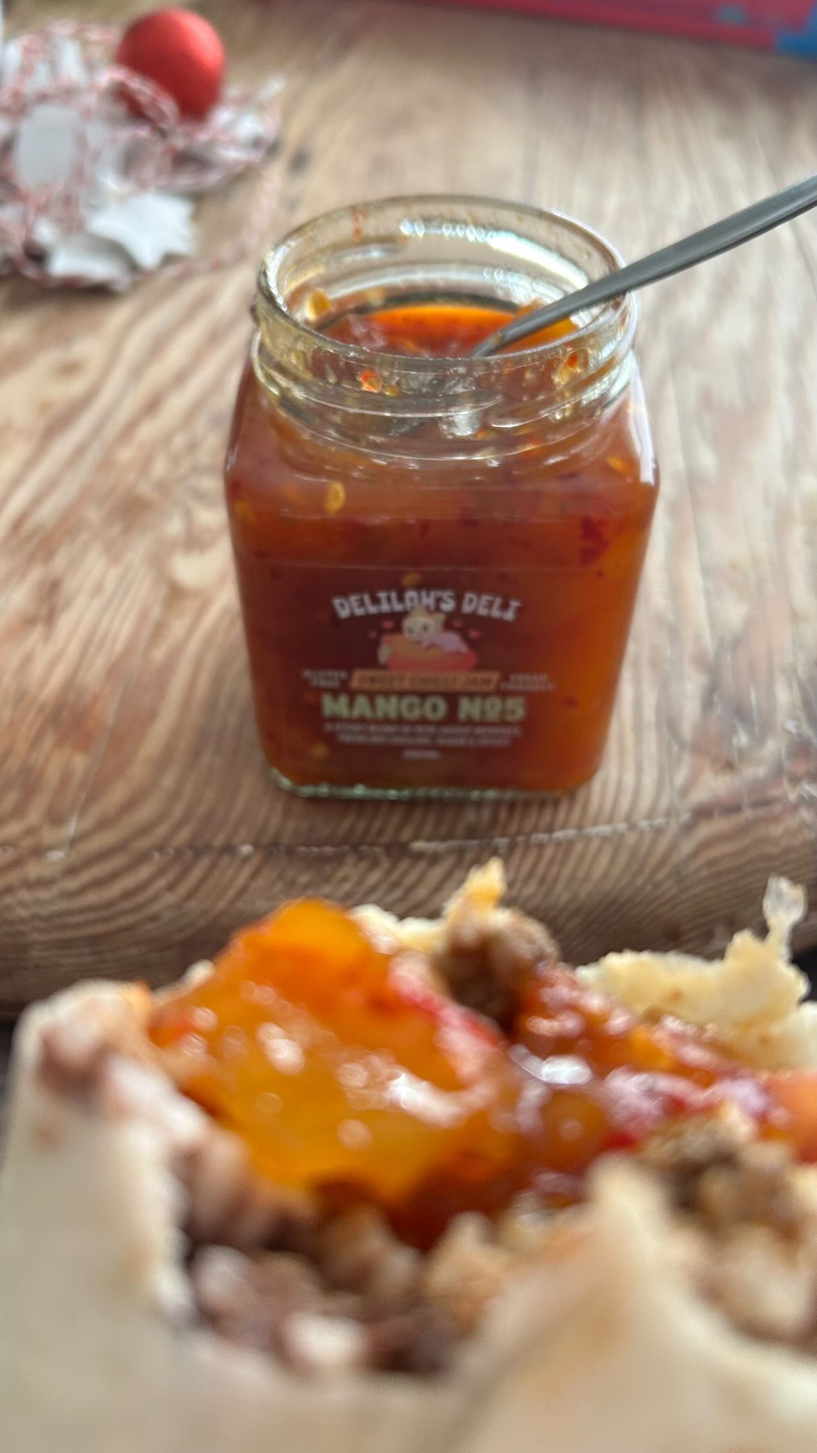 Jar of Delilah's Deli Mango jam on a wooden surface with food in the foreground