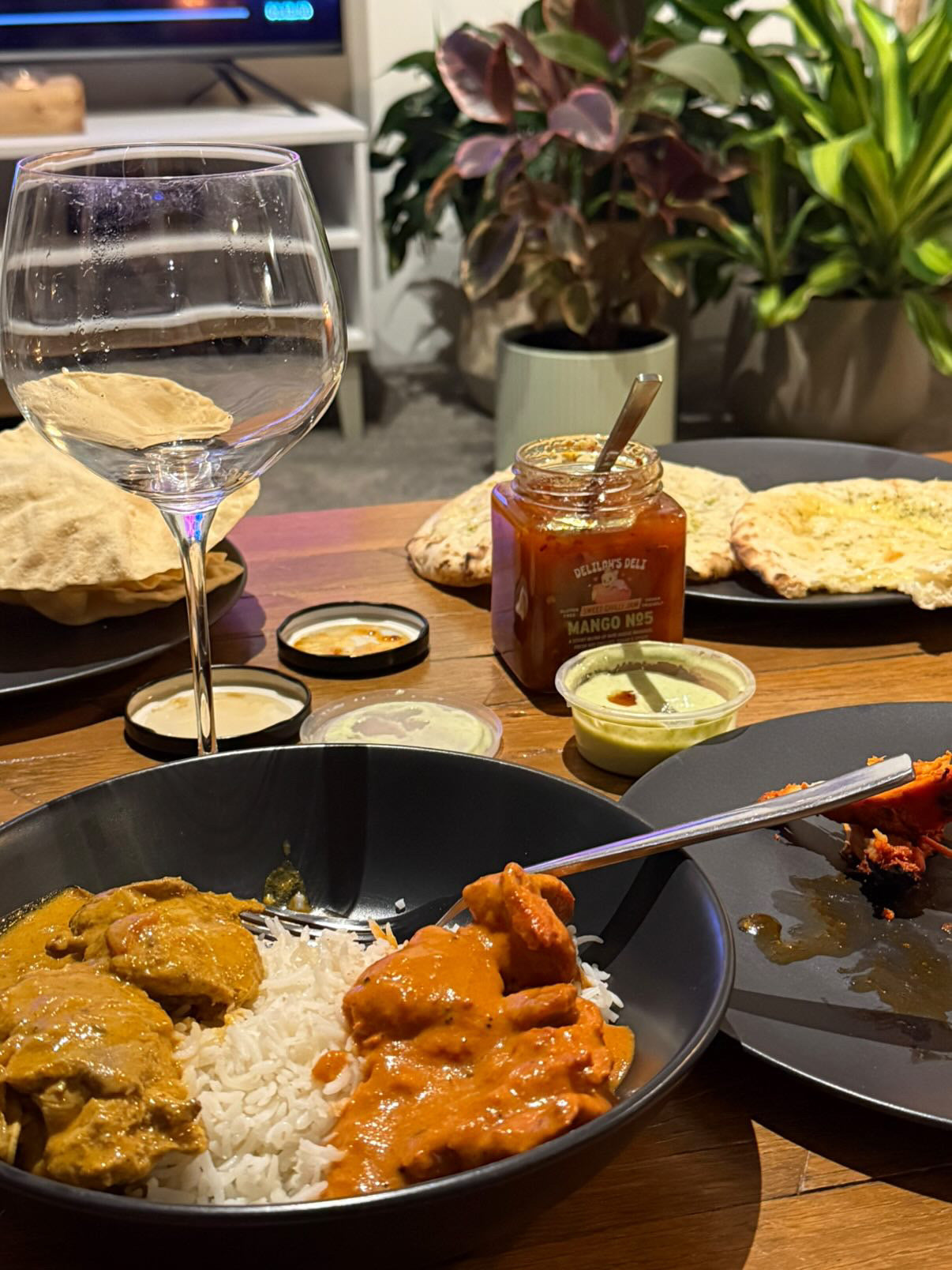 Dinner table with curry, rice, naan bread, and a glass of water with chilli jam