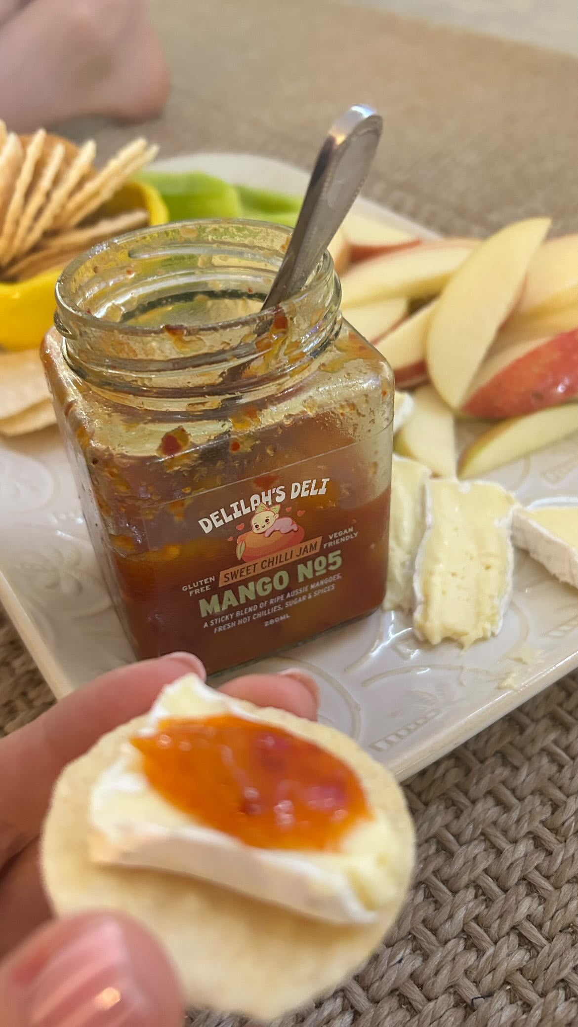 Jar of Delilah's Deli mango jam on a plate with crackers and fruit
