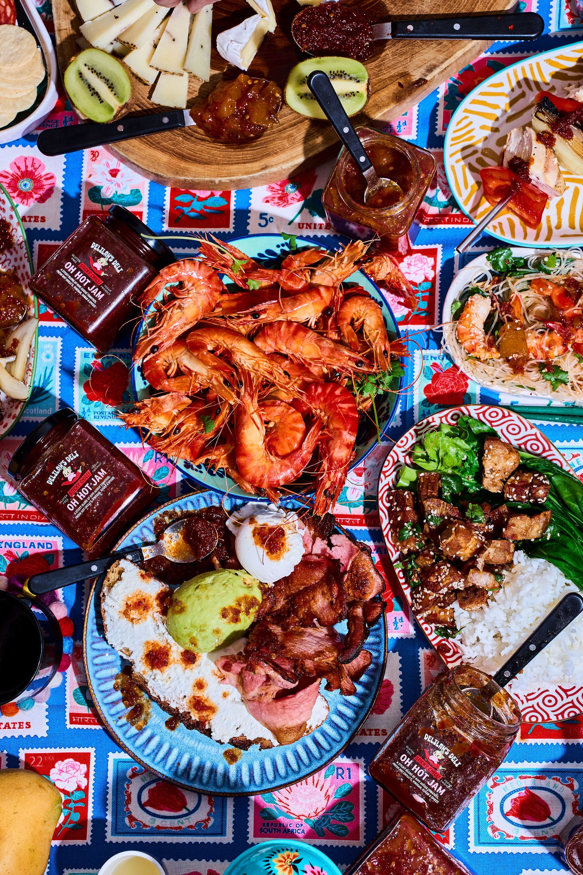 Diverse food platter with prawns, rice, and various dishes on a colorful tablecloth.
