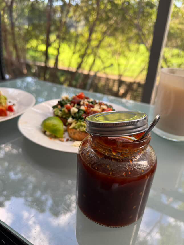 Jar of hot chilli jam sauce with a spoon on a glass table with a blurred outdoor background