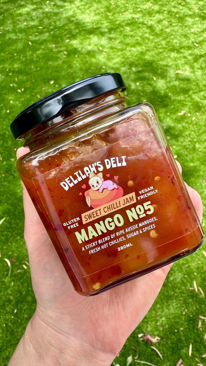 Hand holding a jar of Delly's Deli Sweet Chilli Jam with a green background