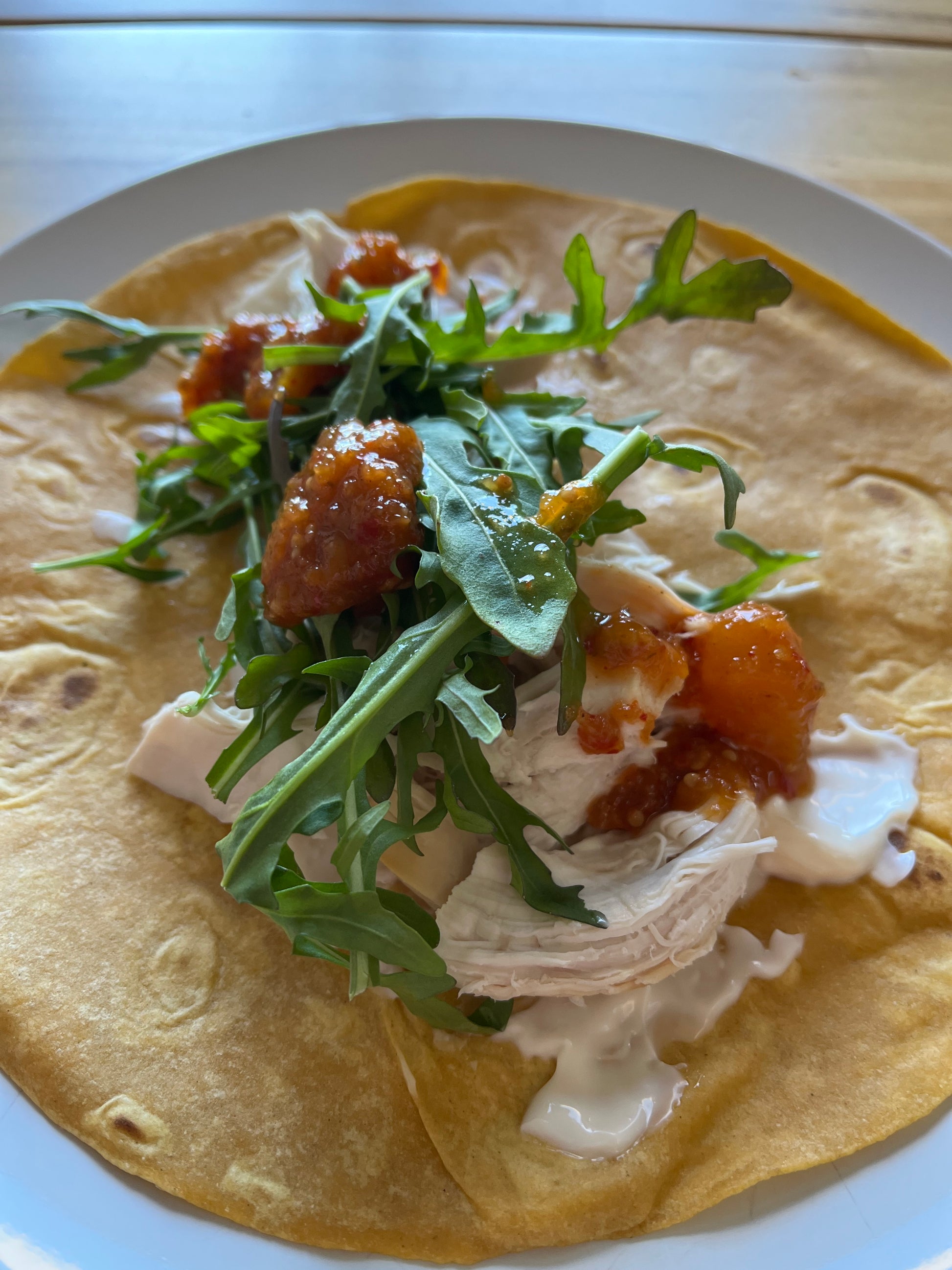 Tortilla with chicken, rocket, and mango sauce on a white plate