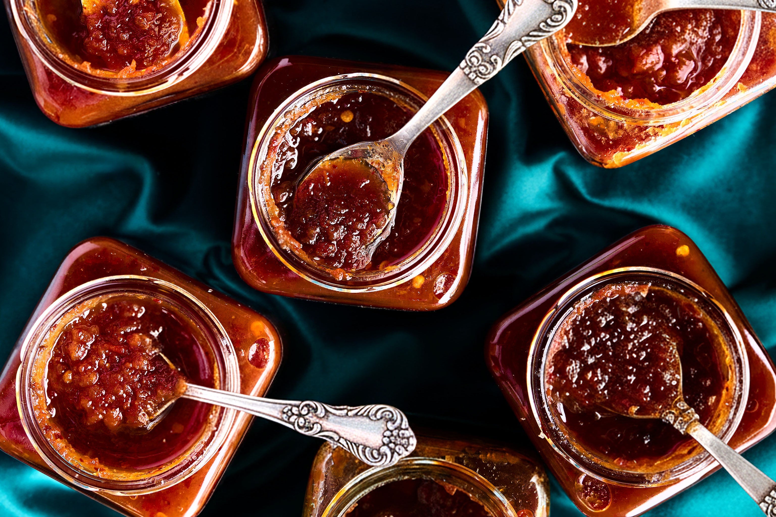 Jars of jam with spoons on a teal fabric background