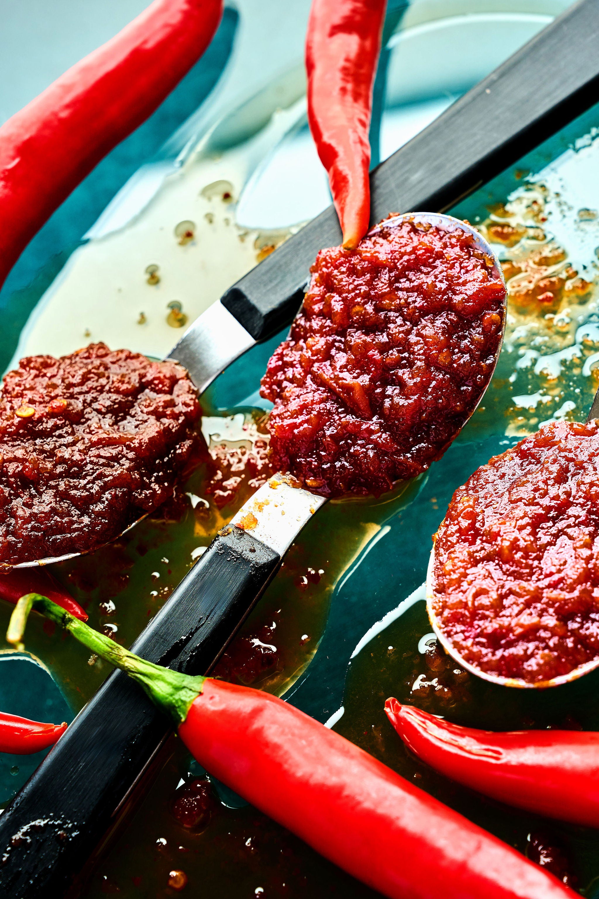 Red chili paste on spoons with red chili peppers on a blue surface