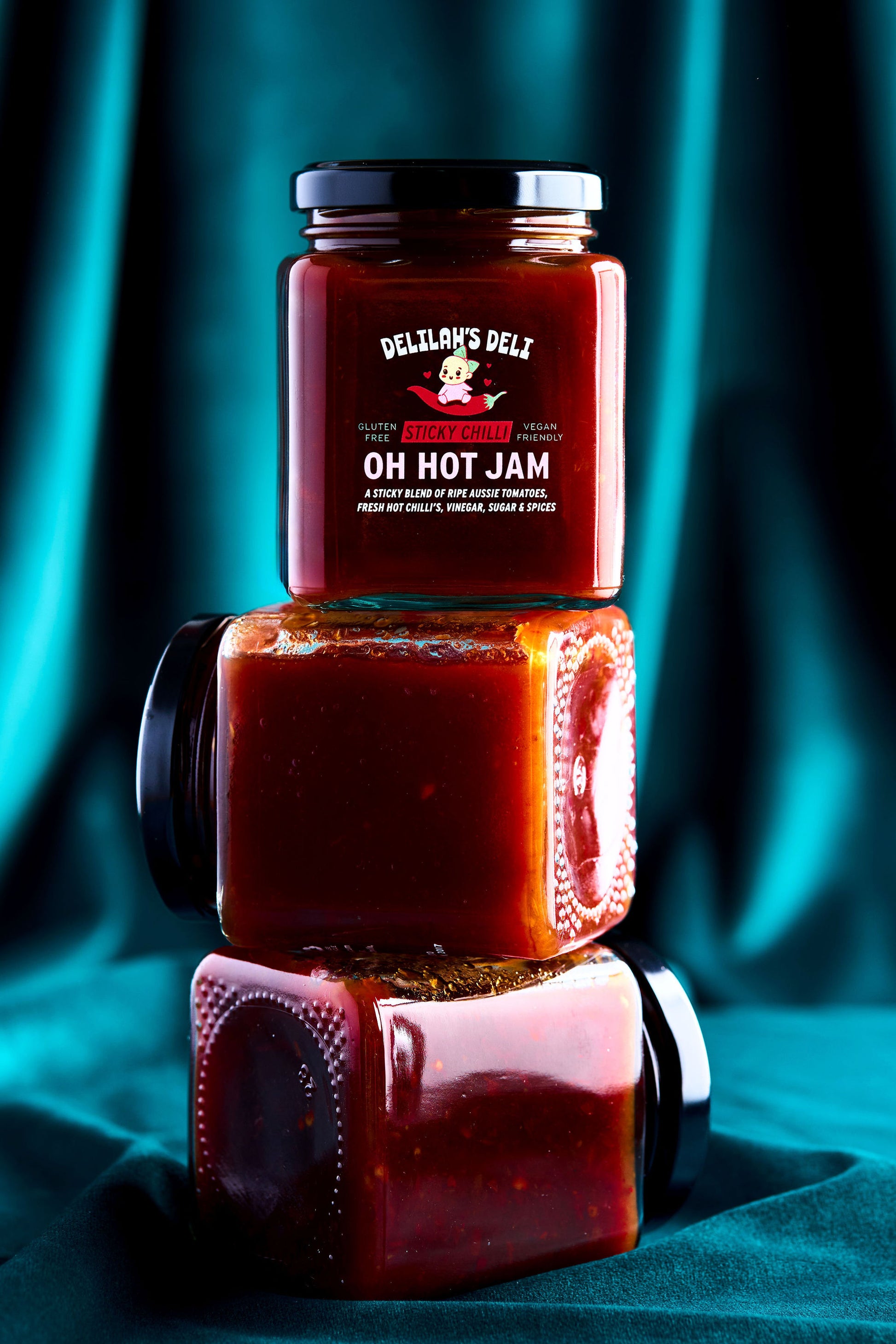 Three jars of Delilah's Deli Oh Hot Jam stacked on a teal fabric background