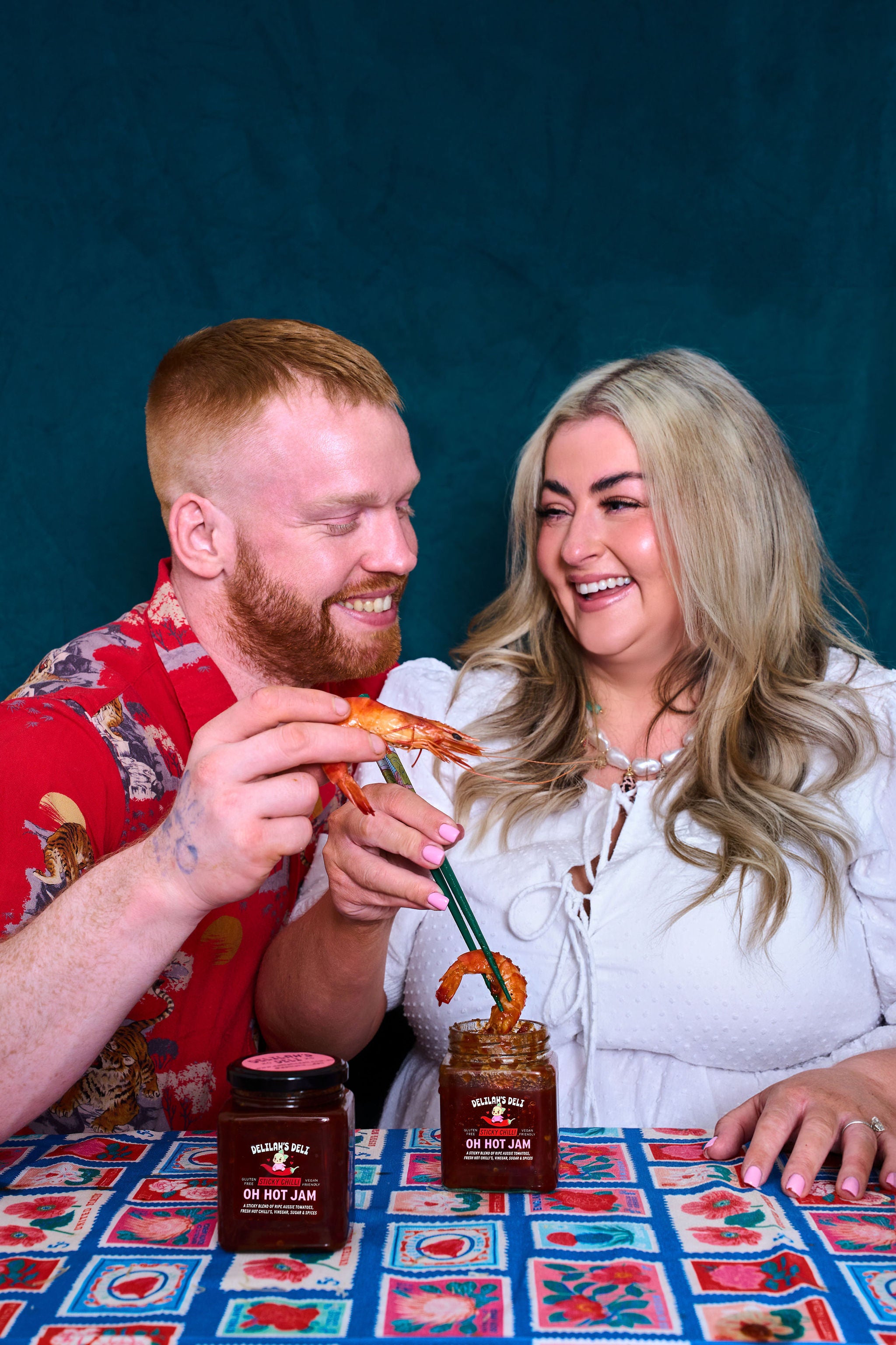 Two people at a table with jars of jam and a blue background