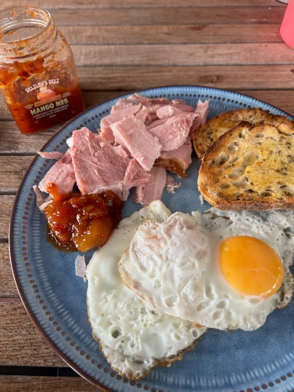 Plate with eggs, ham, toast, and a jar of jam on a wooden surface